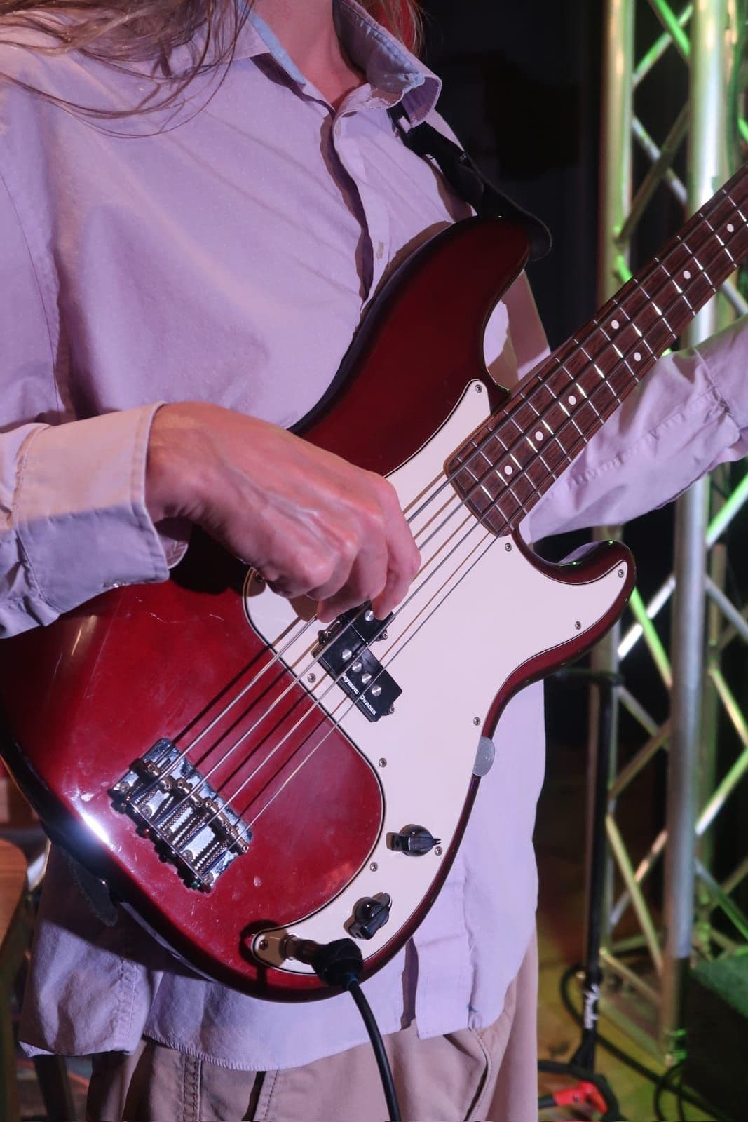 Bassist's hand playing a red bass guitar live