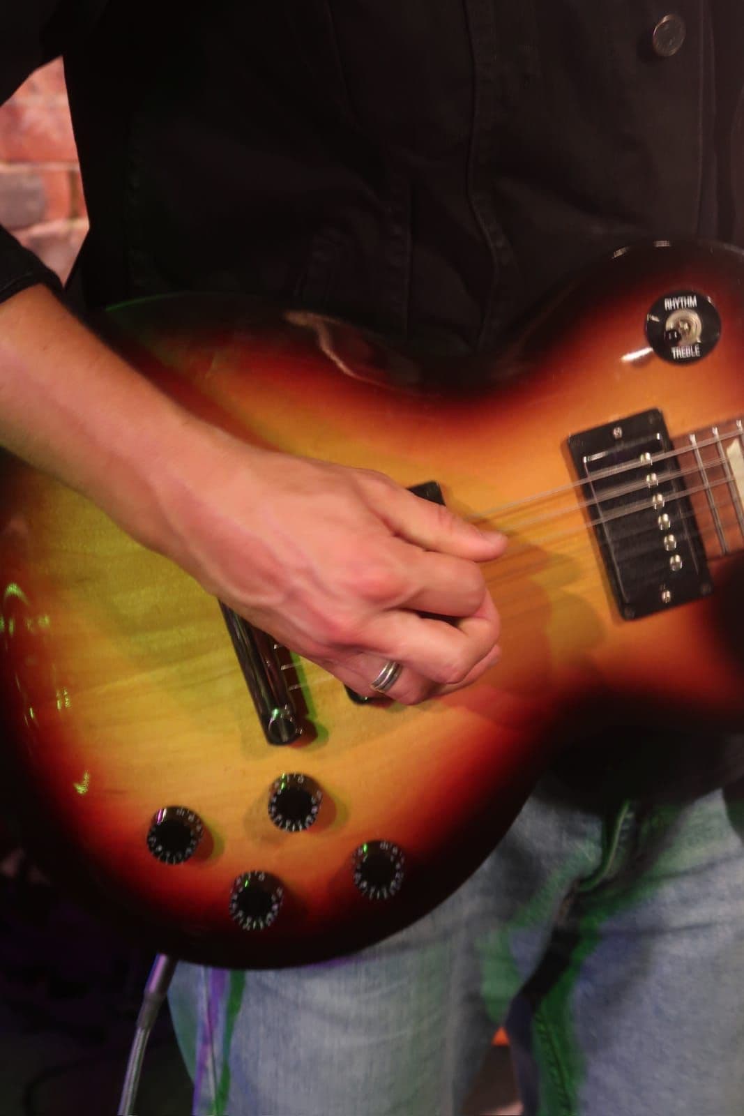 Close-up of a guitarist's hand playing a sunburst guitar on stage