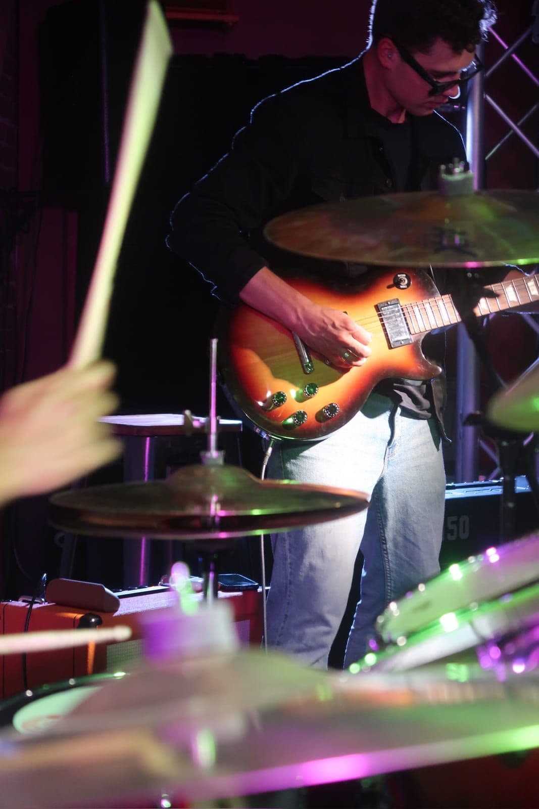 Guitarist playing behind the drum kit's hi-hat and cymbals